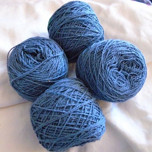 May include: Four balls of blue yarn, each wound into a round shape. The yarn is a medium weight and has a slightly textured surface.