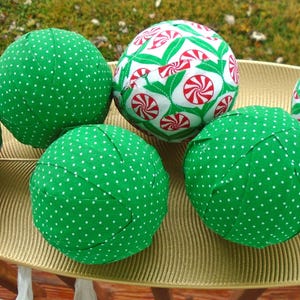 May include: Six fabric Christmas ornaments. Three are solid green with white polka dots, and three have a white background with red and green candy cane designs. The ornaments are displayed on a gold leaf-shaped tray.