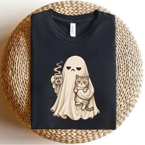 May include: A black crew neck t-shirt featuring a graphic of a beige ghost holding a steaming mug with the text MEH and a power symbol. The ghost is also holding a grumpy-looking brown tabby cat. Two small black bats are visible near the ghost.