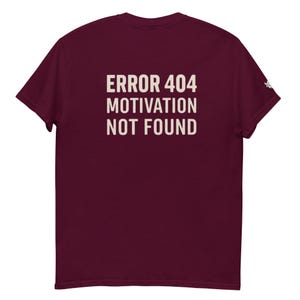 May include: Burgundy t-shirt with the text "ERROR 404 MOTIVATION NOT FOUND" printed in a light beige color. The shirt is a solid color and has short sleeves. The text is centered on the back of the shirt.