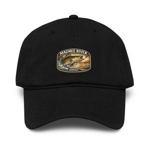 May include: Black baseball cap featuring an embroidered patch with a fish jumping out of the water. The patch reads "Maumee River Ohio" in a curved design. The cap has a curved brim and a button on top.