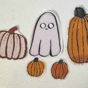 May include: A collection of Halloween-themed patches. The patches include two orange pumpkins, a white ghost with black eyes, and two pumpkins with brown and white coloring. The patches have a white border.