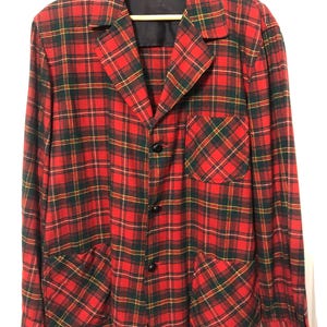 May include: A red, green, and yellow plaid blazer with black buttons and two front pockets. The blazer is hanging on a wooden hanger. A small blue and white tag is visible near the collar.