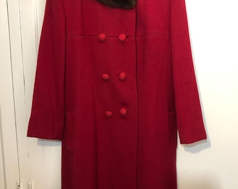 Puede incluir: Un abrigo rojo vintage con cuello de piel marrón y botones rojos grandes. El abrigo es cruzado y cuelga de una percha de madera. El abrigo parece estar hecho de una mezcla de lana.