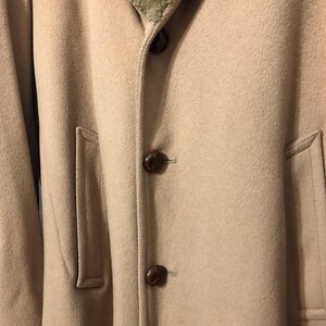 May include: A tan overcoat featuring a brown fur collar and dark brown buttons. The coat has two front pockets and a classic design, suitable for cold weather. The coat is made of a soft, wool-like material.