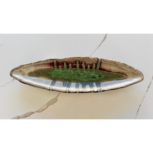 Könnte beinhalten: Eine handgefertigte Keramik-Servierschale mit länglicher Form. Die Schale hat einen zentralen grünen Bereich mit strukturierter Oberfläche, umgeben von einem beigen Rand mit roten und blauen Akzenten. Die Schale ist etwa 30 cm lang.