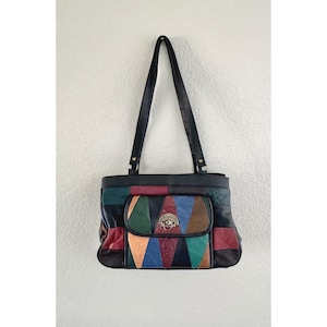 Puede incluir: Un bolso de hombro con un diseño de patchwork de paneles de cuero multicolor en negro, rojo, azul, verde y beige. El bolso incluye dos correas negras, un bolsillo frontal con solapa y cierre metálico circular, y un logotipo central.