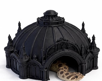 May include: A matte black reptile hide shaped like a domed building with arched doorways and pointed turrets. A tan and brown patterned hognose snake is partially emerging from the central arched entrance of the structure.