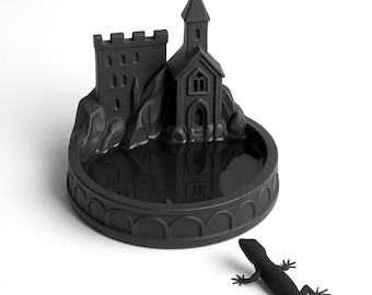 Peut inclure: Un plateau circulaire noir mat présentant une structure sculptée de château et d'église sur un côté, avec un bassin lisse et réfléchissant. Une petite figurine de lézard noir assortie est placée à l'extérieur du plateau, face aux éléments.