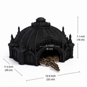May include: A black, dome-shaped reptile hide with architectural details, measuring 12.6 inches wide, 11.4 inches deep, and 7.1 inches high, with a 3.1-inch wide entrance. A brown and black patterned snake is partially emerging from the entrance.