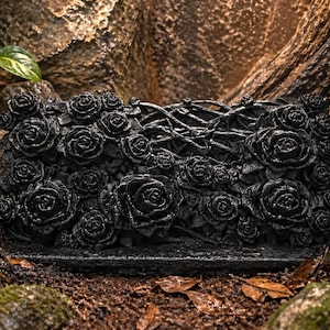 May include: A black, rectangular decorative item adorned with numerous rose blooms. The floral arrangement is set against a backdrop of natural elements, including rocks, moss, and foliage, creating a striking contrast.