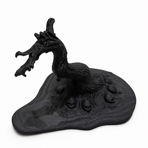 May include: A black sculpture of a dragon-like creature with a textured body and head, perched on a base with several small skulls. The sculpture has a detailed, gothic aesthetic.