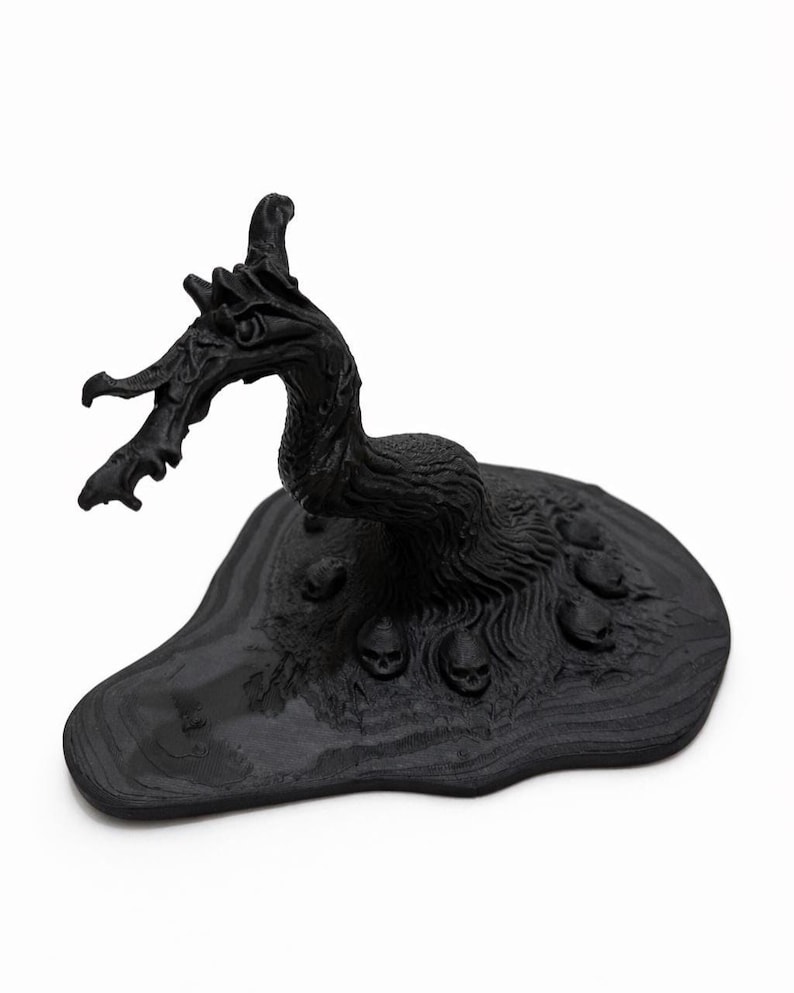 May include: A black sculpture of a dragon-like creature with a textured body and head, perched on a base with several small skulls. The sculpture has a detailed, gothic aesthetic.