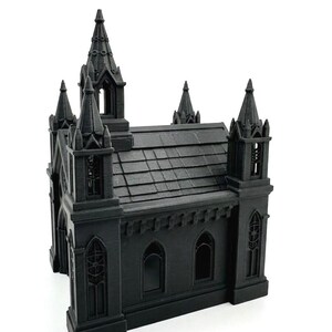 Puede incluir: Modelo de iglesia g&oacute;tica en miniatura de color negro con detalles arquitect&oacute;nicos. El modelo tiene m&uacute;ltiples agujas, ventanas arqueadas y un techo texturizado. El dise&ntilde;o general es sim&eacute;trico y se encuentra sobre un fondo blanco.