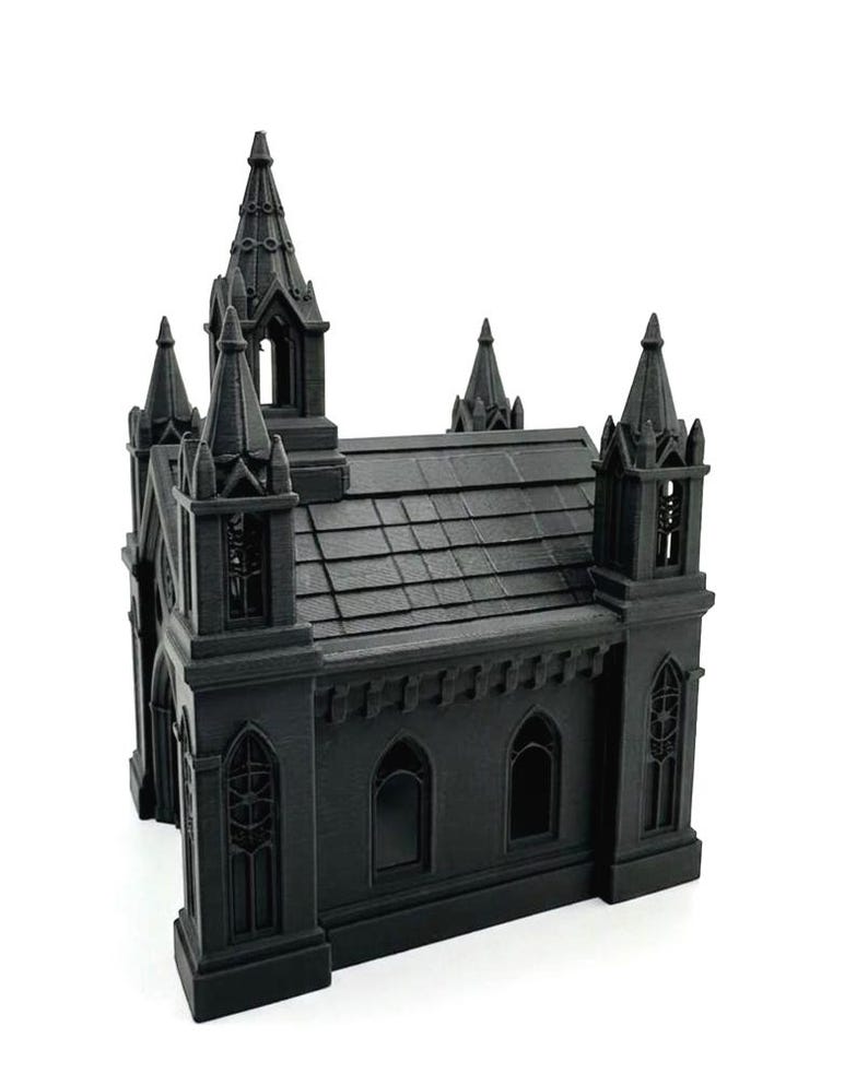 Puede incluir: Modelo de iglesia g&oacute;tica en miniatura de color negro con detalles arquitect&oacute;nicos. El modelo tiene m&uacute;ltiples agujas, ventanas arqueadas y un techo texturizado. El dise&ntilde;o general es sim&eacute;trico y se encuentra sobre un fondo blanco.