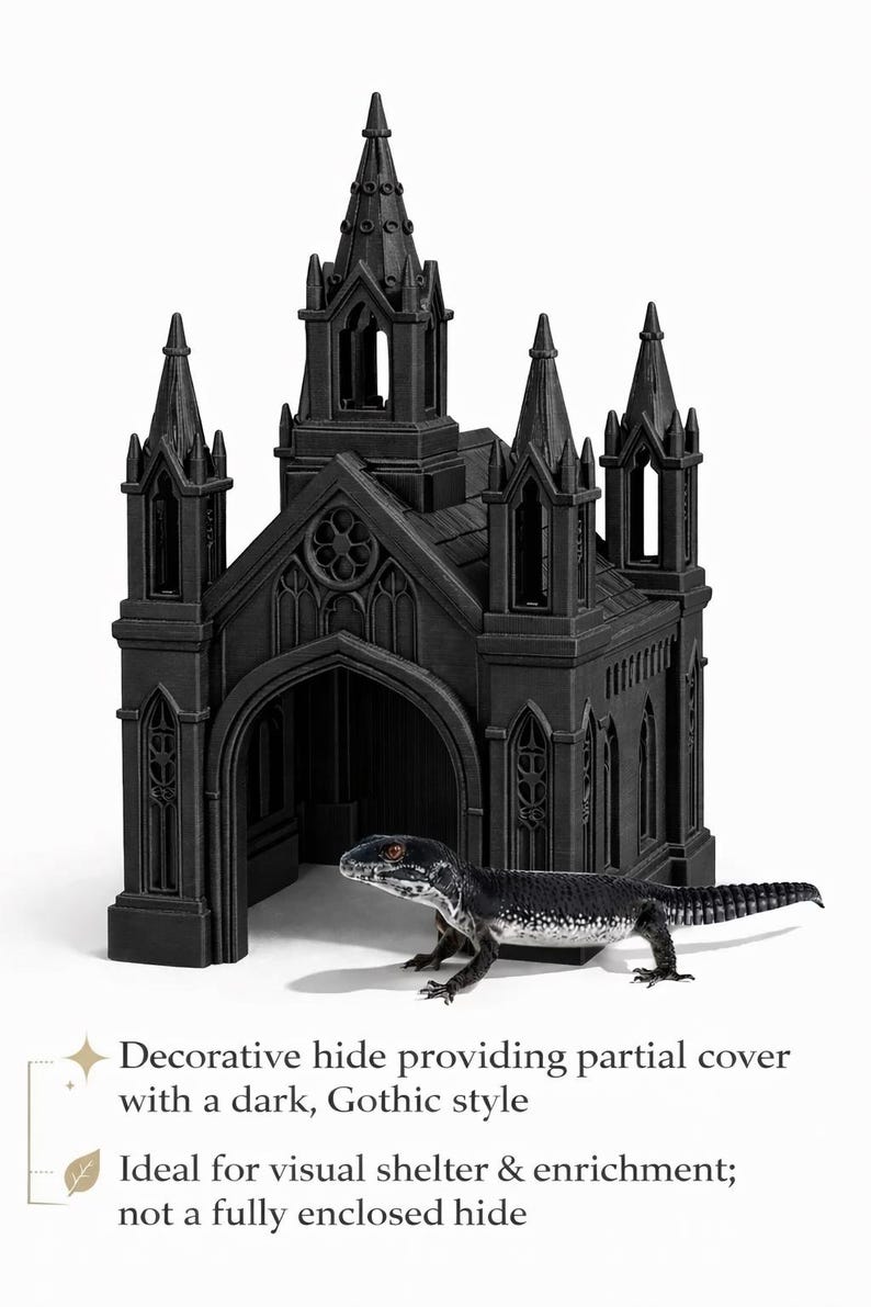 Puede incluir: Escondite decorativo negro de estilo g&oacute;tico para reptiles, que se asemeja a una iglesia en miniatura con agujas y puertas arqueadas. Un lagarto blanco y negro est&aacute; posicionado frente al escondite. El texto de la imagen dice: "Escondite decorativo que proporciona cobertura parcial con un estilo g&oacute;tico oscuro."