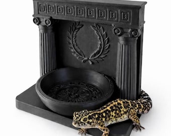 Peut inclure: Un bol d'alimentation pour reptile noir mat au style architectural, doté de deux colonnes cannelées, d'une frise à motif grec et d'une couronne de laurier en relief. Un gecko léopard tacheté de jaune et de noir repose sur la base.