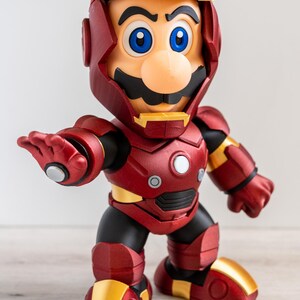 Pu&ograve; includere: Una statuina di Mario in un'armatura di Iron Man. La figura &egrave; principalmente rossa e dorata, con dettagli neri. Il volto di Mario &egrave; visibile, con i suoi caratteristici baffi, naso e occhi blu. La figura &egrave; in posa con un braccio teso.
