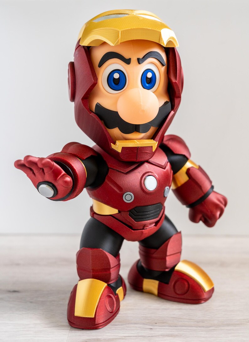 Pu&ograve; includere: Una statuina di Mario in un'armatura di Iron Man. La figura &egrave; principalmente rossa e dorata, con dettagli neri. Il volto di Mario &egrave; visibile, con i suoi caratteristici baffi, naso e occhi blu. La figura &egrave; in posa con un braccio teso.