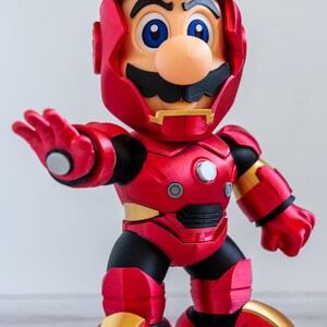 Pu&ograve; includere: Una action figure rossa e oro di un personaggio che &egrave; un mix tra Mario e Iron Man. La figura ha un'armatura rossa con dettagli dorati, un elmo dorato e la faccia di Mario. La figura &egrave; in posa con un braccio teso.