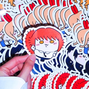 May include: A die-cut vinyl sticker featuring a cartoon character with bright orange hair, yellow spiral eyes, and a white collared shirt with a black tie. The character is depicted with a small, simple facial expression and is holding up one finger.