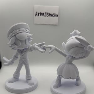 May include: Two white 3D-printed figurines. One figure is in a military-style uniform and hat, reaching out to touch the hand of a figure in a dress and hat. Both figures are on circular bases. The text "ArmsSmasher" is visible.
