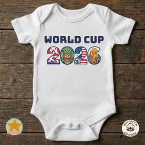 Op de afbeelding: Witte babybody met de tekst "WORLD CUP 2026" in marineblauw. De cijfers zijn versierd met vlaggen en symbolen. De body is gemaakt van 100% katoen.