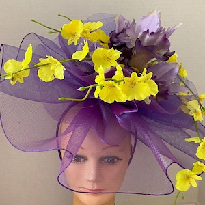 May include: A purple hat with a sheer, ruffled brim, adorned with yellow orchids and purple irises. The hat is designed with a headband and a decorative bow, perfect for special occasions.