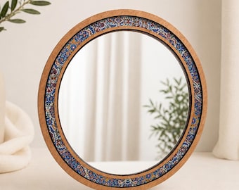 Può includere: Uno specchio rotondo decorativo con cornice in legno. La cornice è adornata da un colorato motivo a mosaico in blu, rosso e giallo. Lo specchio riflette uno sfondo neutro.