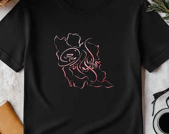 Può includere: T-shirt nero con un design rosa a linea continua. La grafica è un'illustrazione astratta di una persona con un cappello. La maglietta è realizzata in materiale morbido e ha maniche corte. La maglietta è esposta su una superficie di legno bianco.