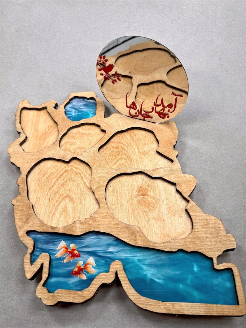 May include: Wooden decorative tray in the shape of a country, featuring a blue resin river with goldfish. An oval wooden piece with red text and a floral design sits atop the tray. The tray has several cut-out sections.