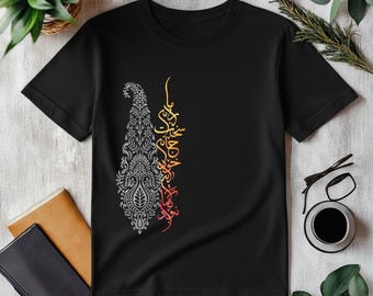 Può includere: T-shirt nero con un motivo paisley grigio sul lato sinistro e calligrafia sul lato destro. La calligrafia è in giallo, arancione e rosso. La maglietta è esposta su una superficie bianca. Il motivo paisley è dettagliato.