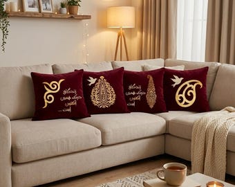 Può includere: Un set di quattro cuscini bordeaux con disegni dorati e testo su un divano angolare beige. I cuscini presentano vari motivi, tra cui un paisley, un uccello e un disegno astratto. La stanza è decorata con una mensola in legno, una lampada e un tappeto.