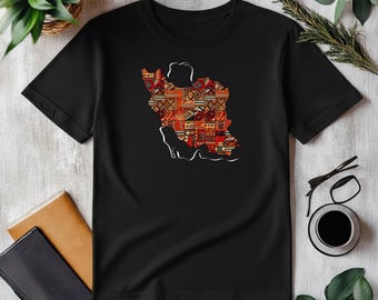 Può includere: T-shirt nero con un contorno bianco di una mappa di un paese riempita con un design colorato. Il design incorpora forme geometriche rosse, arancioni e marroni. La maglietta è esposta su una superficie bianca con altri oggetti.