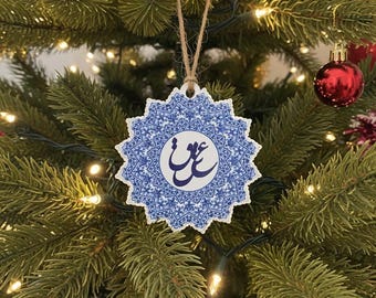 Può includere: Un ornamento natalizio in ceramica blu e bianca con un design a stella e calligrafia araba. L'ornamento è appeso a uno spago di spago naturale su uno sfondo di un albero di Natale decorato con ornamenti rossi e luci.