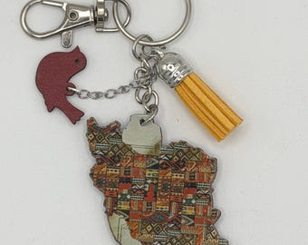 Può includere: Portachiavi con una mappa dell'Iran, decorato con un colorato motivo a tappeto. Ha un piccolo ciondolo a forma di uccello rosso, un nappa gialla e un moschettone e un portachiavi argentati. Il design della mappa presenta un motivo dettagliato.