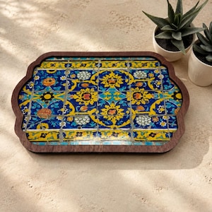 May include: A rectangular wooden tray with rounded, scalloped edges featuring a vibrant mosaic tile inlay. The tiles display a repeating pattern of bright yellow, deep blue, and orange floral motifs with intricate black line details.