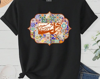 Può includere: T-shirt nero con un design decorativo con motivi geometrici colorati e calligrafia araba. Il design è incorniciato da un bordo arancione-marrone ornato. La maglietta ha maniche corte e un orlo annodato.