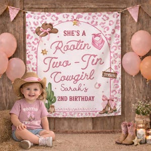 May include: A pink and white leopard print birthday backdrop featuring a brown cowboy hat, a pink bandana, a cactus, and the text 'SHE'S A Rootin Two-Tin Cowgirl Sarah's 2ND BIRTHDAY'. A child wears a straw cowboy hat and a pink t-shirt with matching text.
