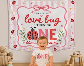 Może przedstawiać: Biało-różowe tło z tkaniny w paski z czerwoną biedronką, białymi stokrotkami i napisem "OUR LITTLE love bug IS TURNING ONE Olivia's birthday". W zestawie pasujące białe body z krótkim rękawem z grafiką biedronki i napisem "ONE".