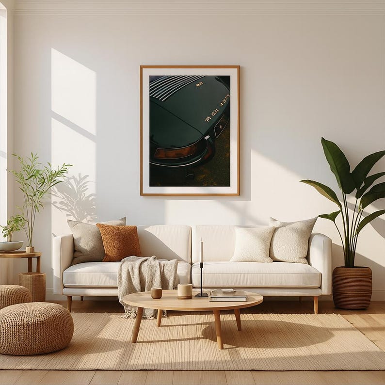 May include: A framed print of a vintage dark green sports car, showcasing the rear with the model name. The image is displayed in a living room setting with a neutral-toned sofa, pillows, and a wooden coffee table.