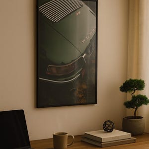 May include: Framed print of a vintage green Porsche car. The image shows the rear of the car with the word "Porsche" visible. The print is displayed on a wall above a wooden desk with a laptop, mug, and books.
