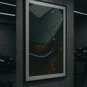 May include: Framed art print featuring a dark green vintage car's rear. The image shows the car's body, with gold lettering spelling out the car's brand name. The print is displayed in a modern garage setting.