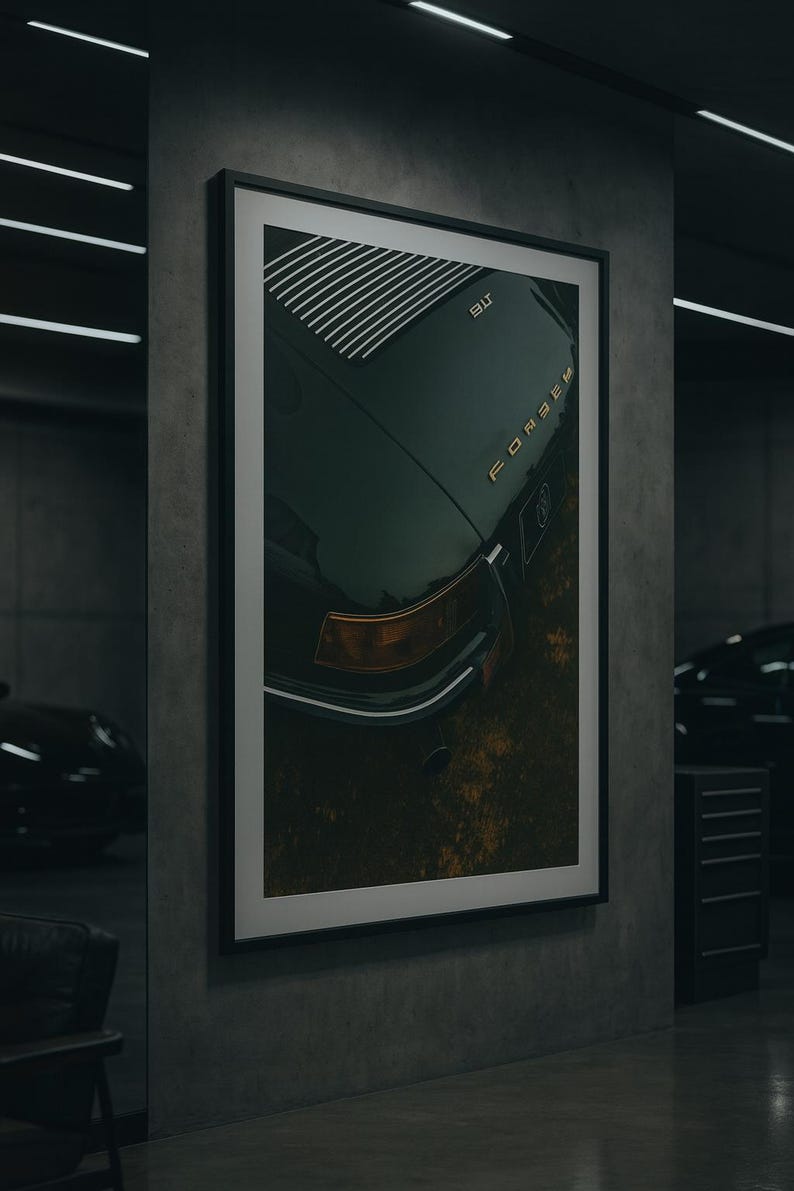 May include: Framed art print featuring a dark green vintage car's rear. The image shows the car's body, with gold lettering spelling out the car's brand name. The print is displayed in a modern garage setting.