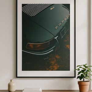 May include: Framed art print featuring a close-up of a vintage dark green Porsche. The car's rear, with the word "Porsche" in gold lettering, is the focal point. The image has a vintage aesthetic, with a focus on the car's design and details.