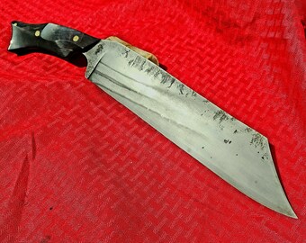 May include: A large, silver knife with a black handle and brass accents. The blade is slightly curved and has a dull finish. The knife is lying on a red fabric background.