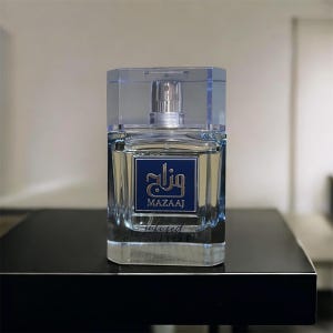 Puede incluir: Un frasco de perfume de vidrio transparente con un atomizador plateado y una tapa azul. El frasco tiene una etiqueta azul con escritura árabe y la palabra "MAZAAJ" en dorado. La palabra "infused" está impresa debajo.