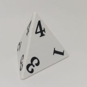 May include: A white four-sided pyramid-shaped die featuring black numerals printed on each of its triangular faces. The visible numbers include 1, 2, 3, and 4, each displayed in a bold, serif font style on the smooth, matte-finished surfaces.