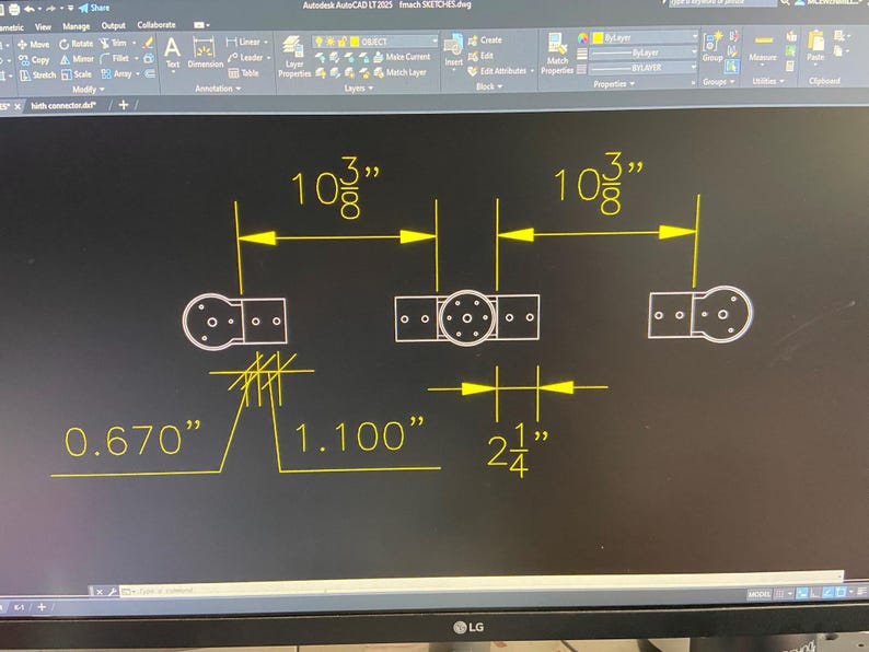 May include: A technical drawing on a black screen, featuring a detailed mechanical design. Dimensions are provided in inches: 10 3/8", 0.670", 1.100", and 2 1/4". The design includes circular and rectangular shapes with multiple holes.