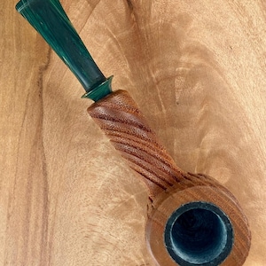 May include: A tobacco pipe featuring a natural brown wooden bowl with a textured, spiraled stem and a smooth, dark green marbled acrylic mouthpiece. The bowl has a circular opening with a dark interior, and the stem connects to the mouthpiece.